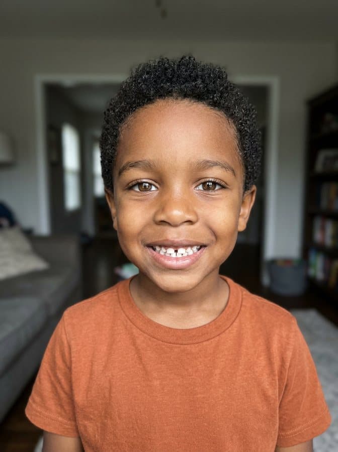Photo of Maximiliano, an invented boy with short tight curls and a gap-toothed grin, made with AI